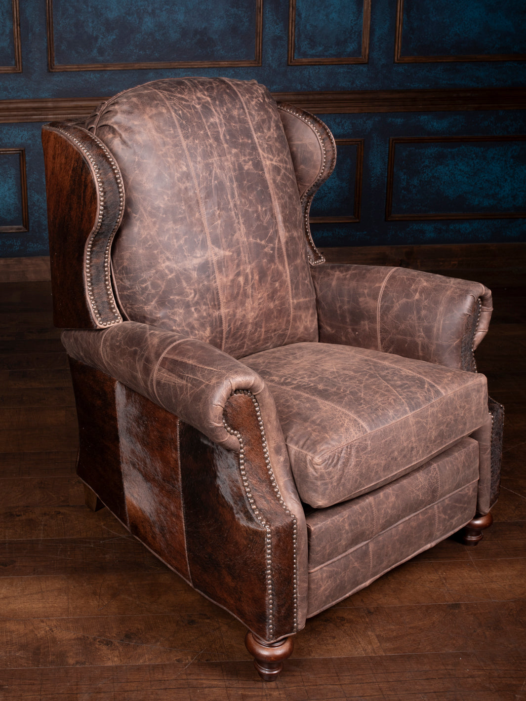 A brown leather recliner with distressed detailing and hair-on-hide accents, set against a dark background.