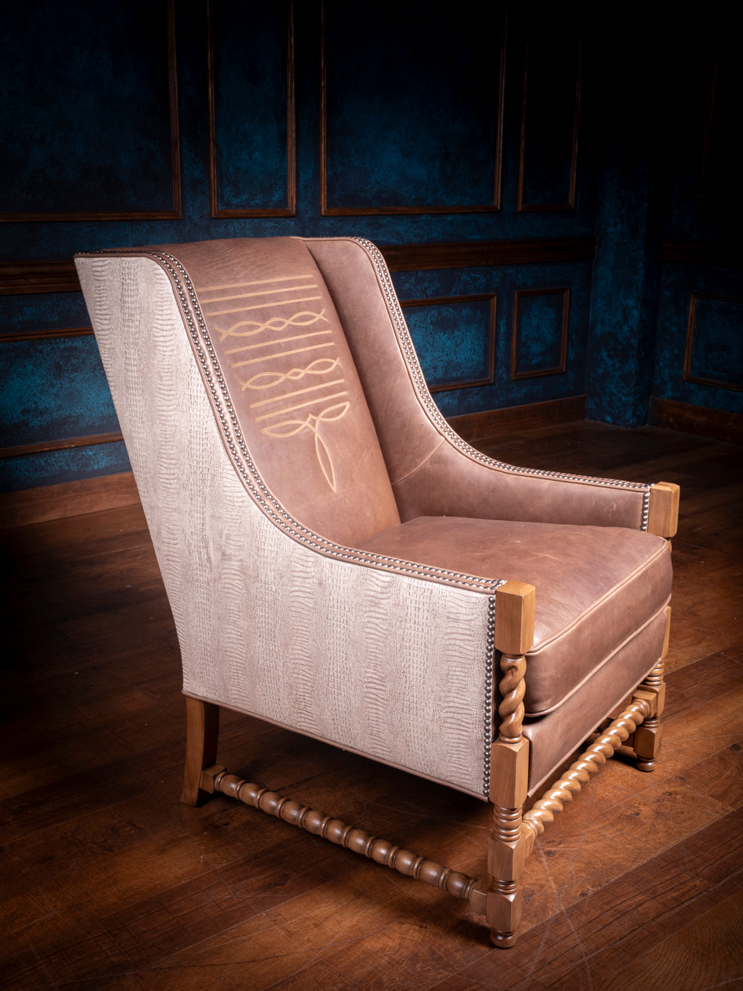 Handcrafted Western leather accent chair featuring tan leather upholstery, intricate stitchwork on the backrest, natural wood twist legs, and textured side panels in a rustic-luxury room setting.