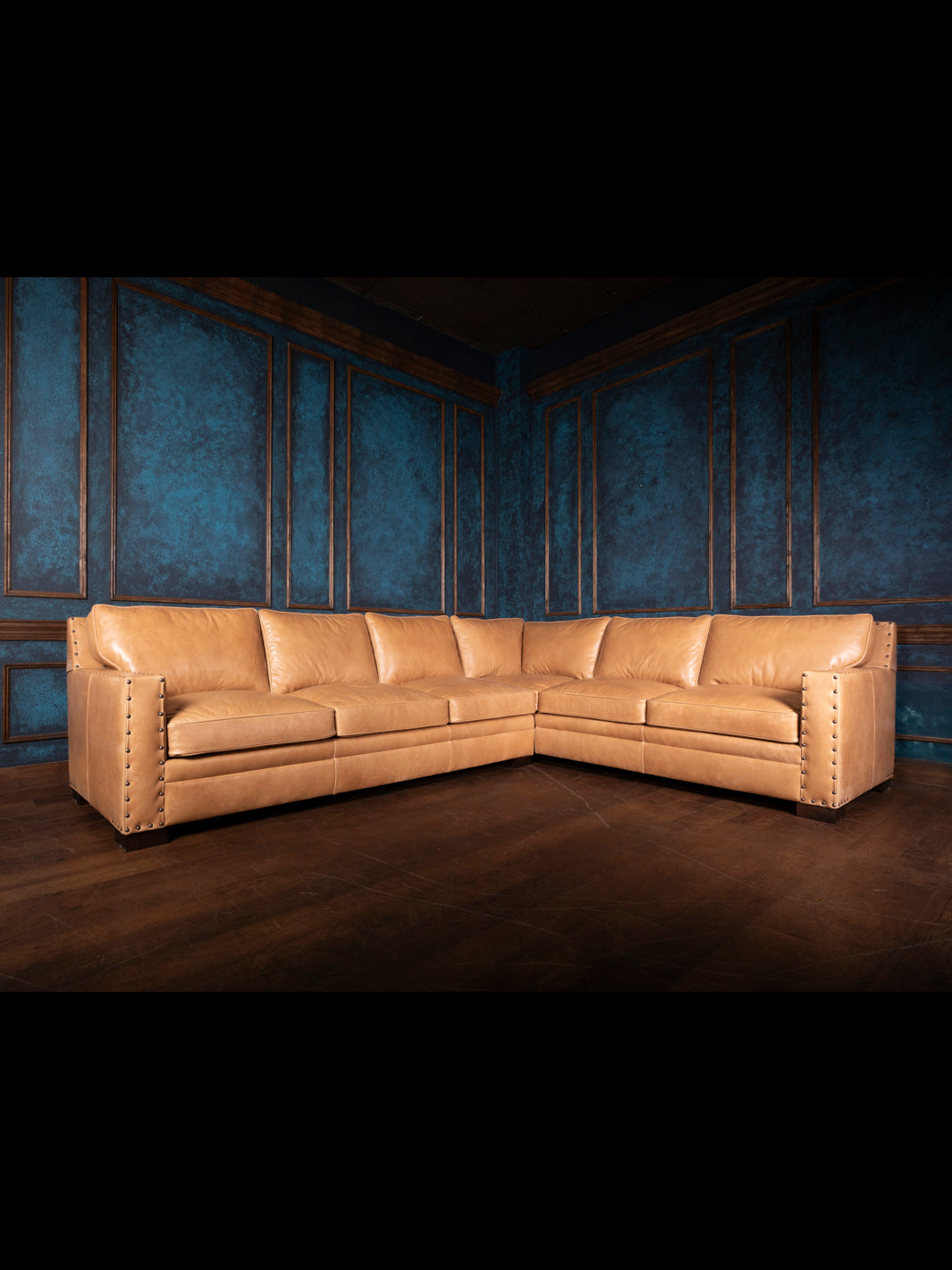 A large, beige leather sectional sofa with a plush texture, situated in a room with blue walls and wooden flooring.