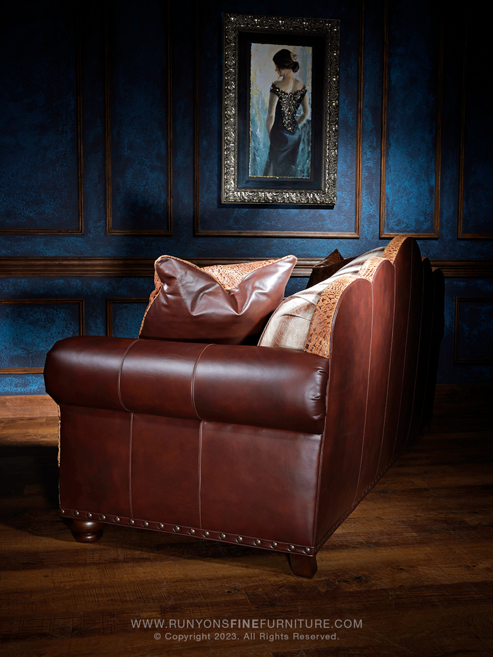 side angle of a rich brown leather sofa with curved arms and vertical seam details, accented by crocodile-embossed leather and soft leather throw pillows.