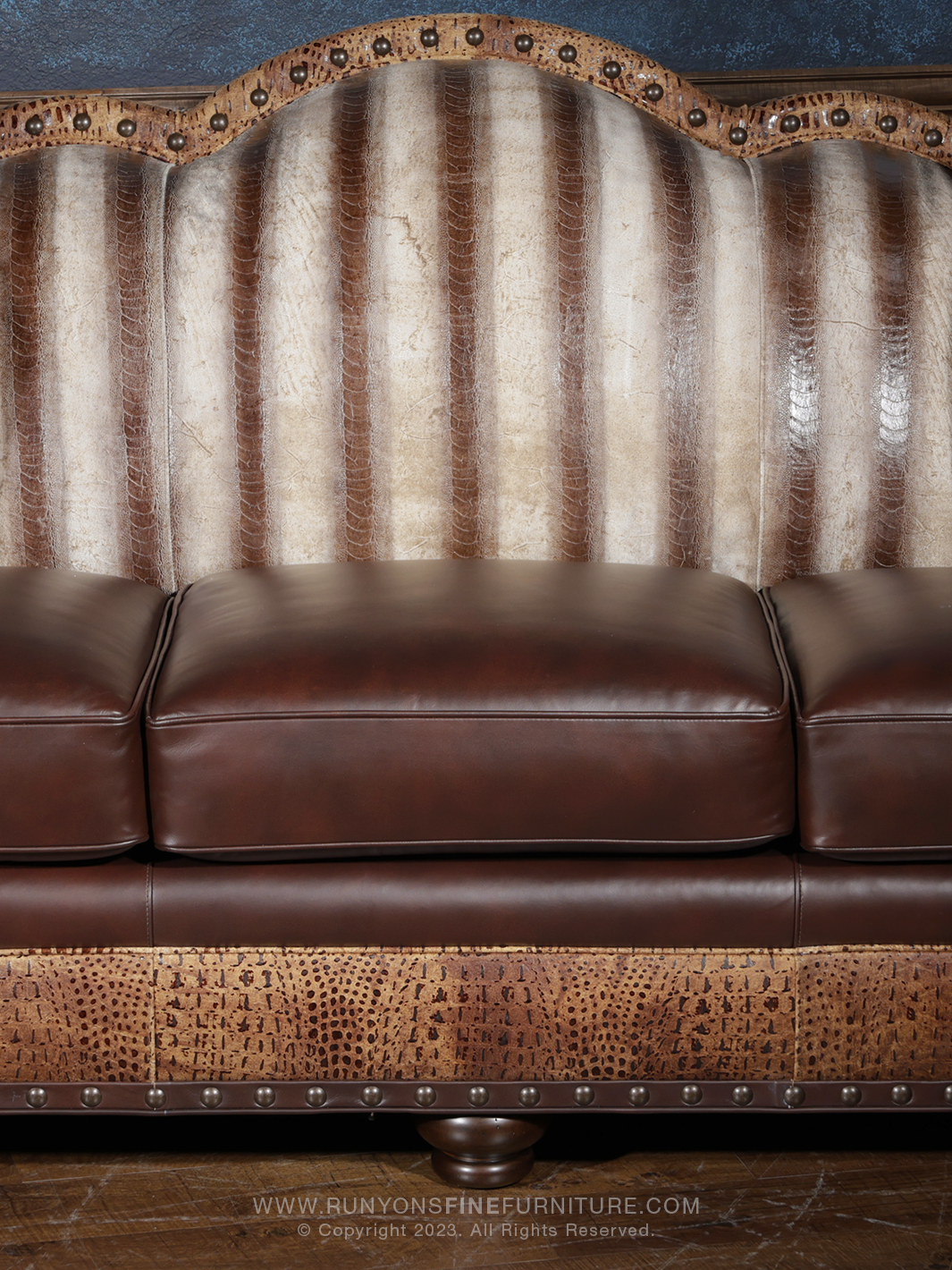Close-up view of a luxury western-style leather sofa featuring vertical ridges of exotic leather on the backrest, with dark brown seat cushions and embossed leather trim on the base.