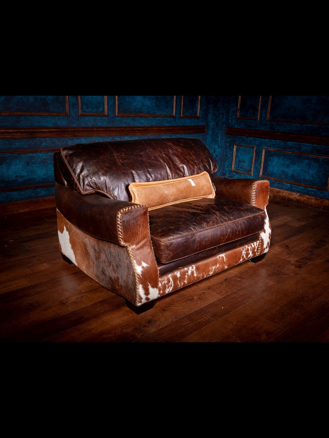 Rustic leather and cowhide chair-and-a-half with wide armrests, oversized back cushion, and contrasting hide panels with hand-laced seams, ideal for Western-style interiors.