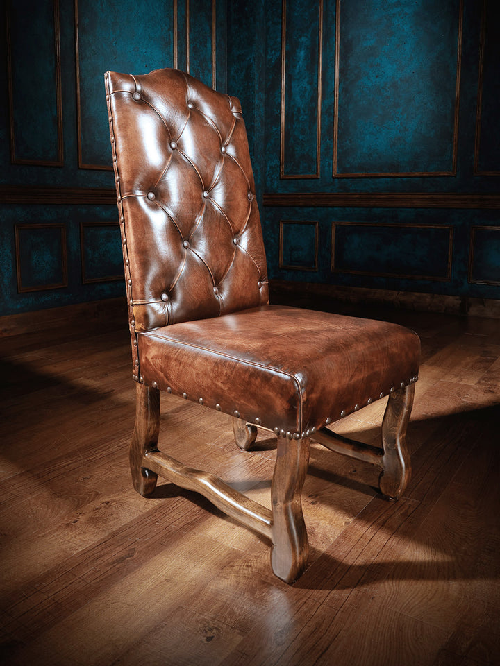 A tufted back leather dining chair with a rustic wooden frame and high-density foam cushion, displayed in a dimly lit room with wood flooring.