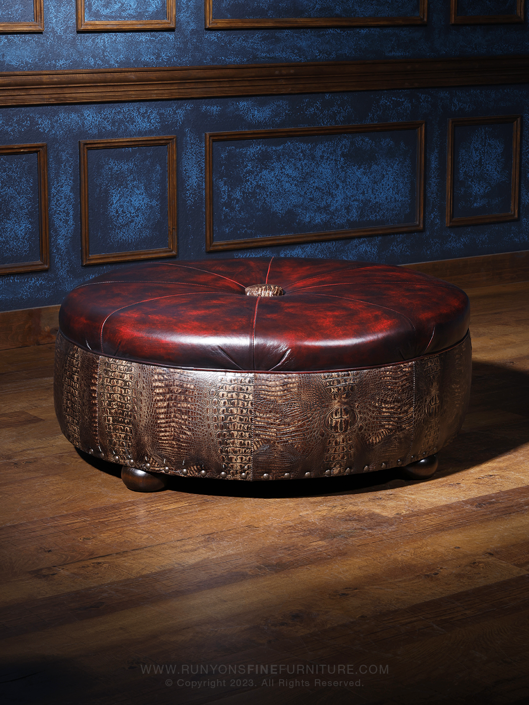 A round red leather ottoman with crocodile pattern embossing, placed on a wooden floor against a blue wall.
