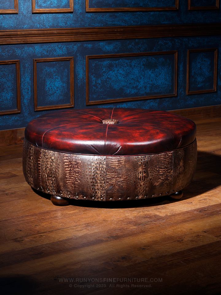 A round red leather ottoman with crocodile pattern embossing, placed on a wooden floor against a blue wall.