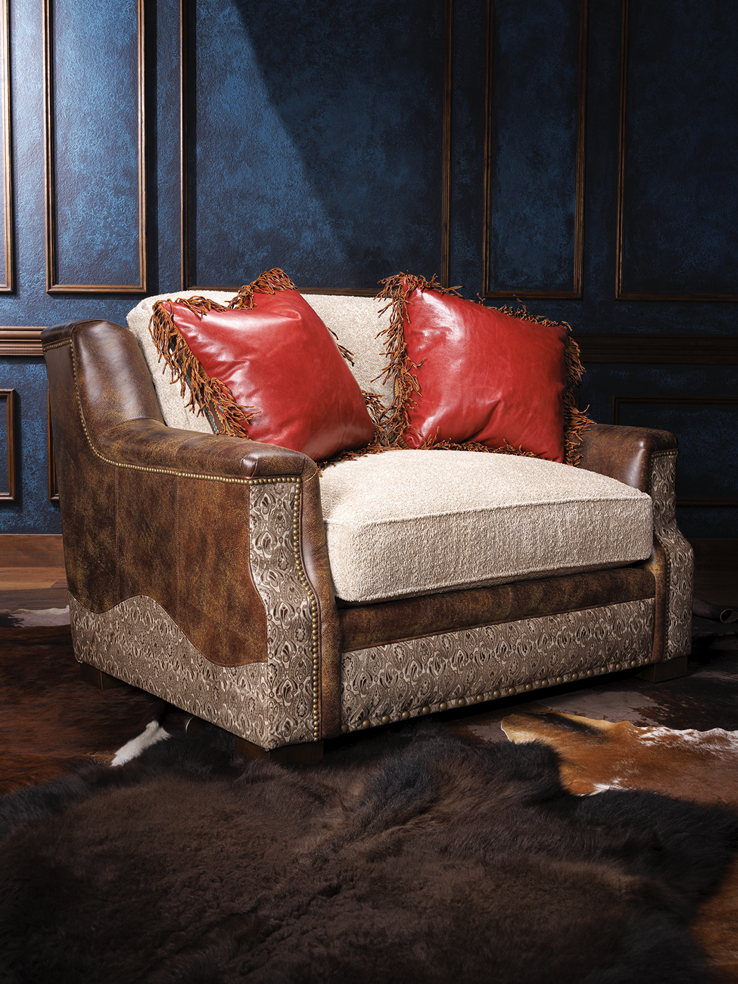 front side view of Armchair with beige fabric and brown leather upholstery, decorated with red leather pillows and ornate side patterns, set against a dark wall.
