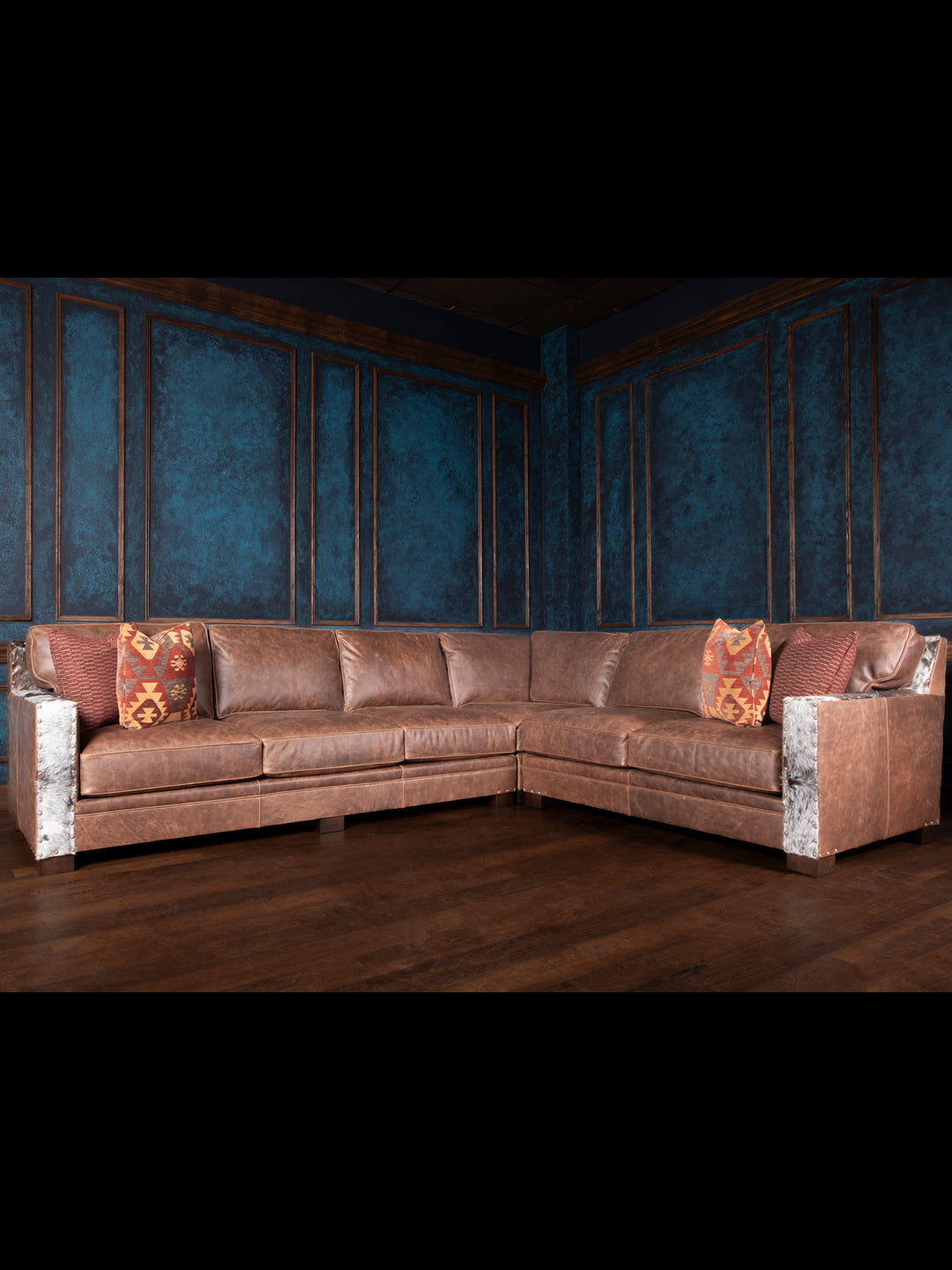 A large, luxurious leather sectional sofa with embossed patterns, situated in a room with blue walls and wooden flooring, accessorized with patterned cushions.