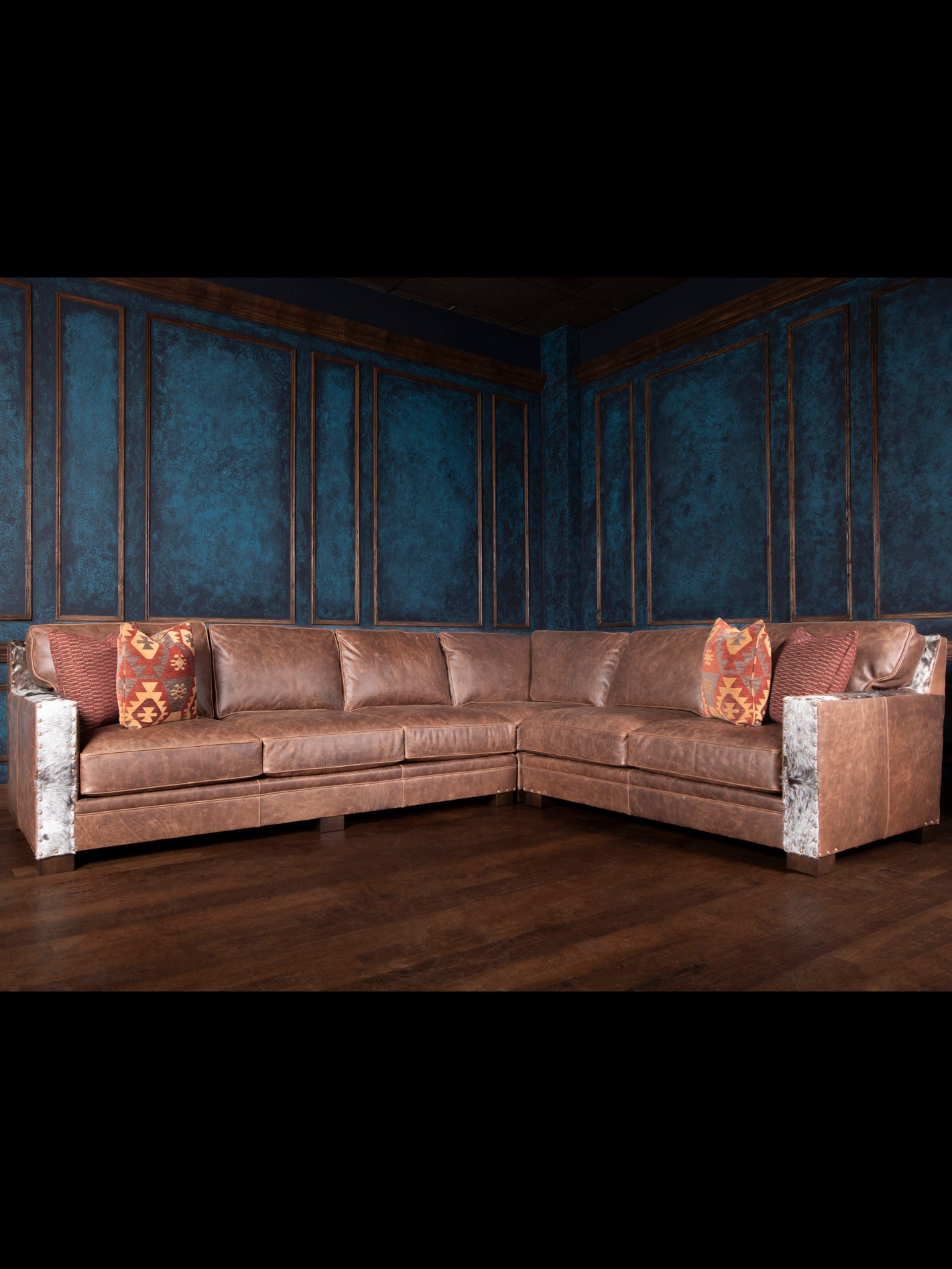 A large, luxurious leather sectional sofa with embossed patterns, situated in a room with blue walls and wooden flooring, accessorized with patterned cushions.
