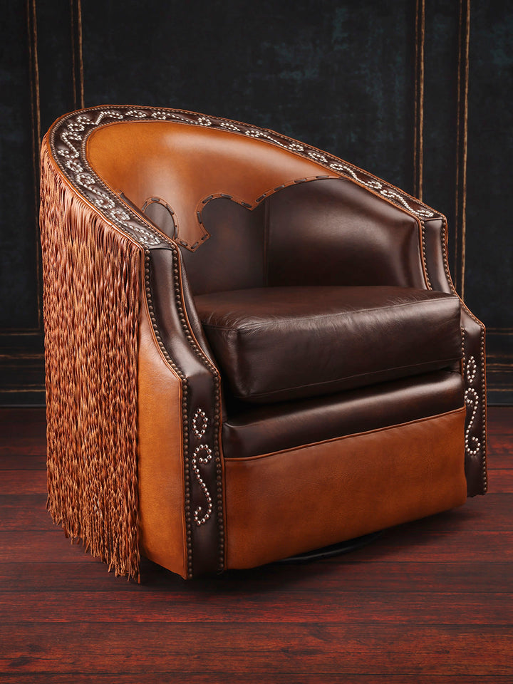 A brown rustic swivel chair with fringe details and leather upholstery, positioned on a wooden floor with dark background.