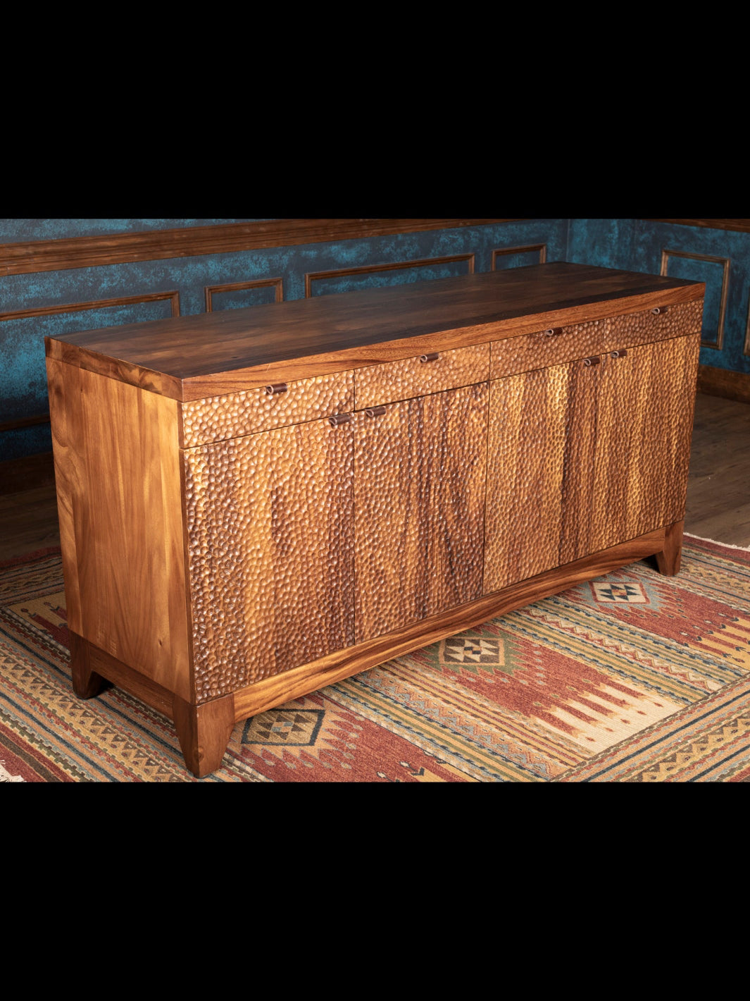 Wooden sideboard with metallic accents in a room with patterned rug and blue walls.