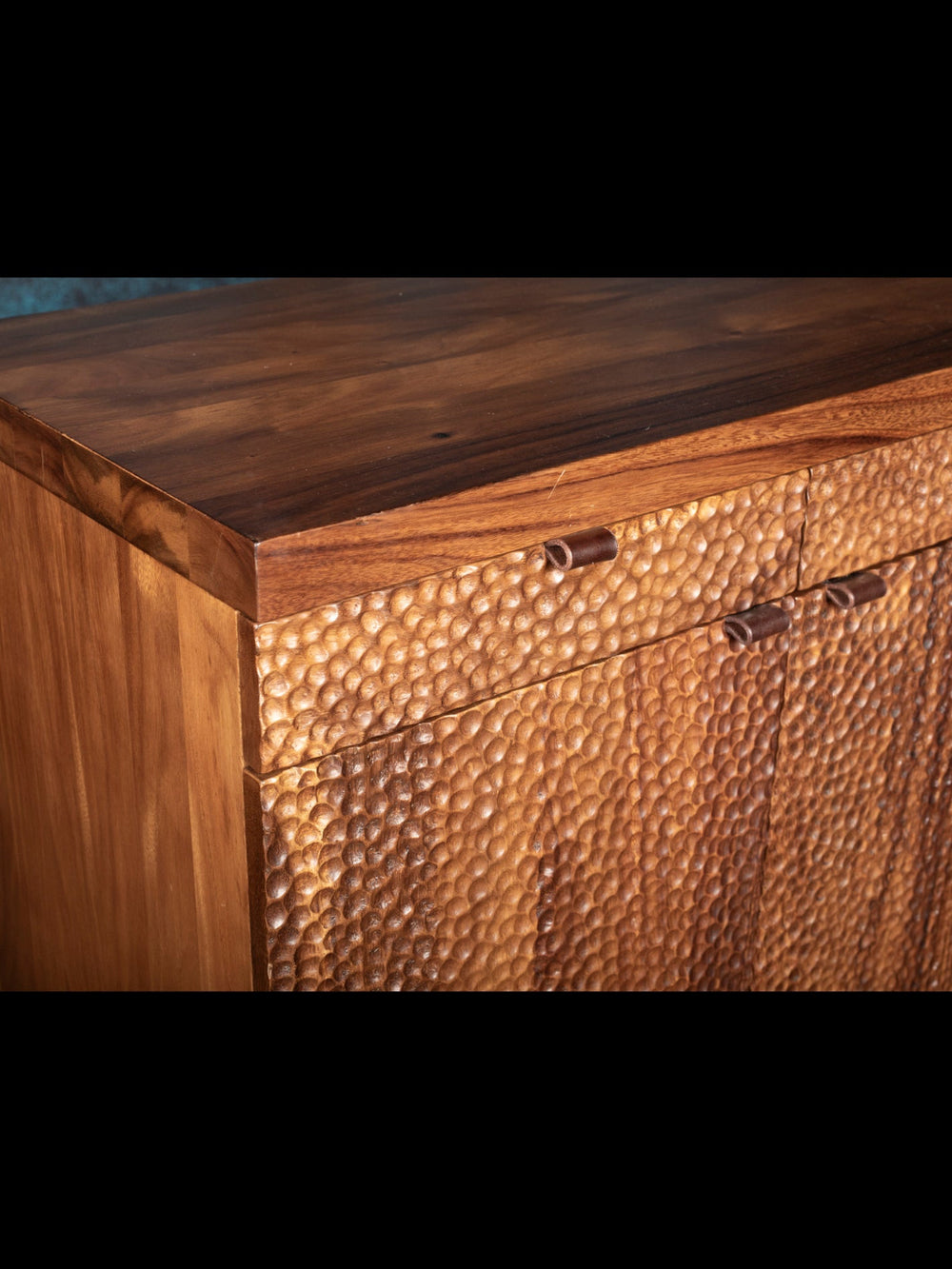 Wooden sideboard with a textured surface and metal handles on a dark background
