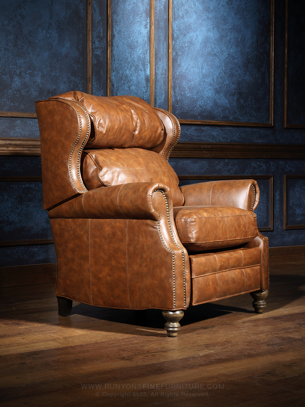 A hazelnut brown leather recliner chair with a classic design, placed in a room with blue paneling.