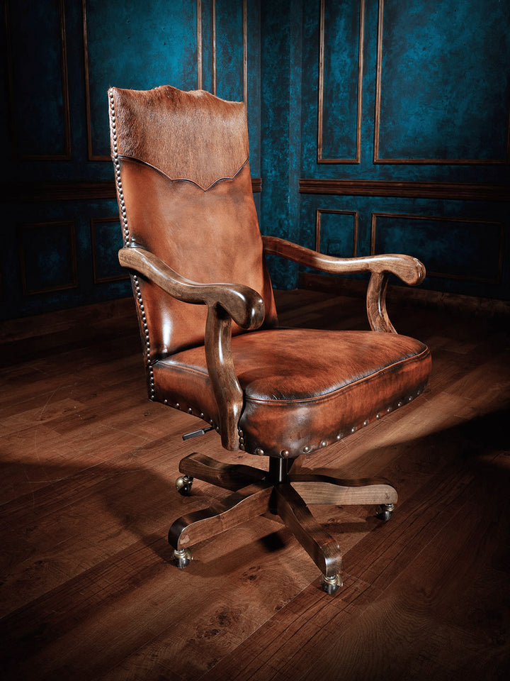 A brown leather desk chair with a wooden frame and metal nailhead trim, equipped with smooth-rolling casters, positioned in a room with blue paneling.