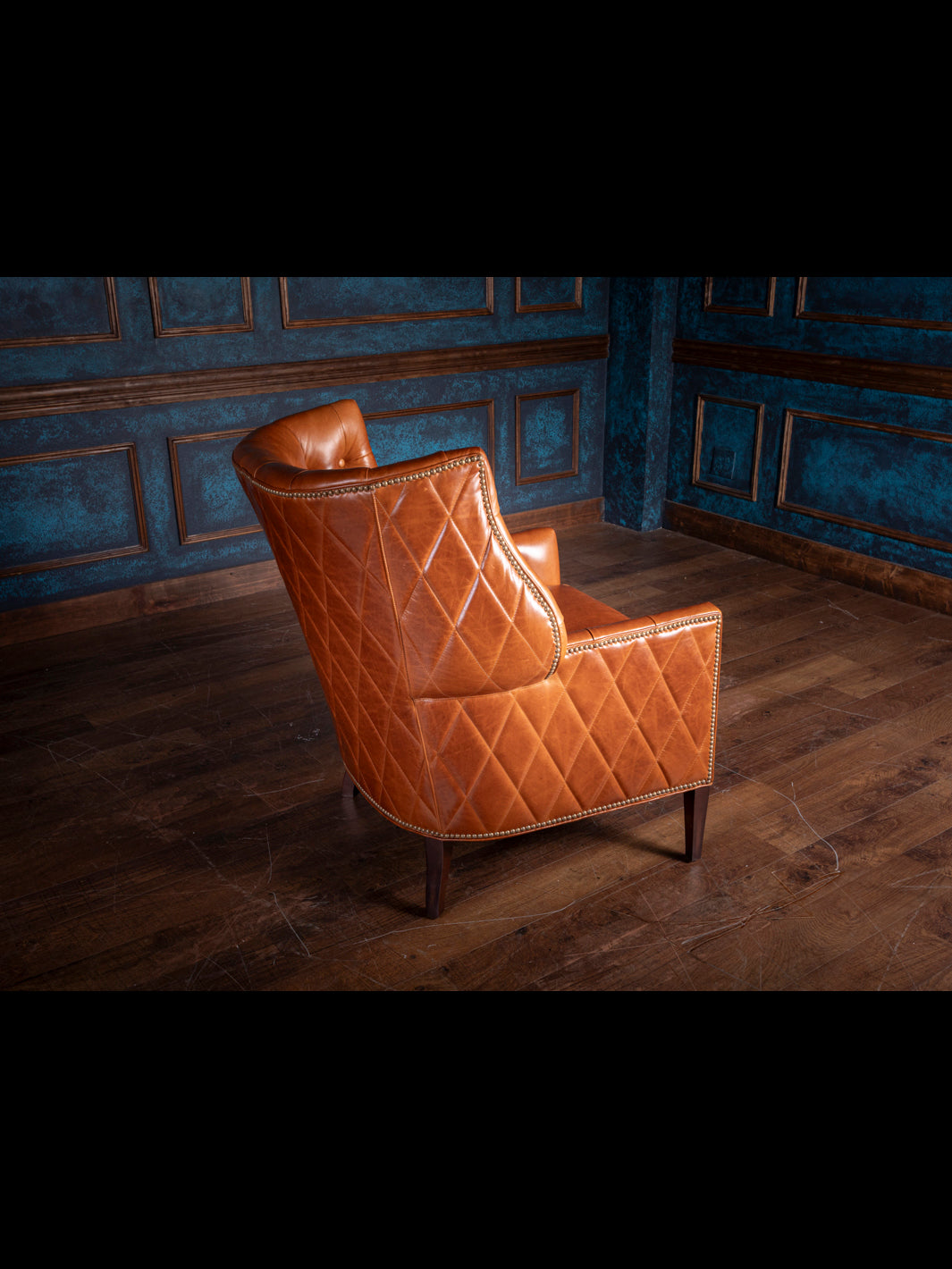 Handcrafted western leather accent chair with a caramel diamond-stitched backrest, shown at an angle to highlight its rich leather texture and dark wood legs