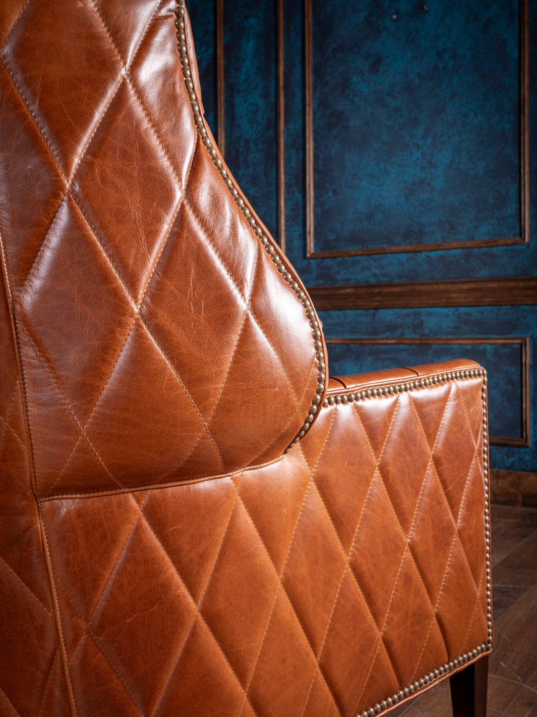 Close-up of a caramel leather accent chair featuring diamond-pattern stitching and bronze nailhead trim, embodying rustic western craftsmanship