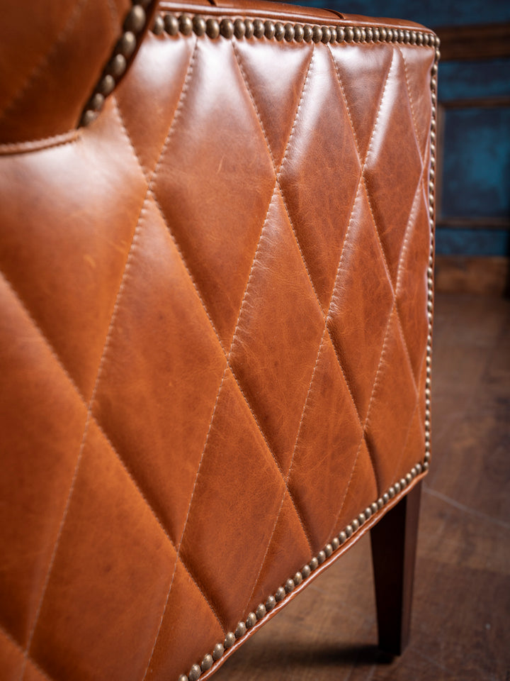 Detail shot of handcrafted western leather accent chair with caramel diamond quilting and antique brass nailhead trim along the edge