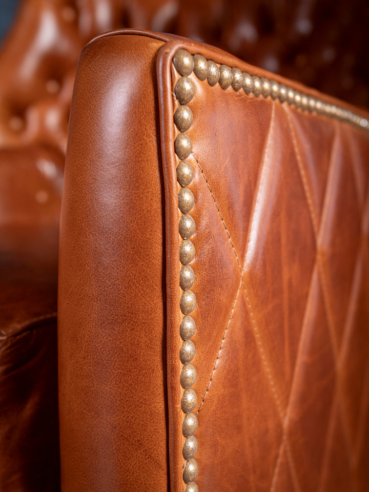 Luxury armrest detail on a handcrafted caramel leather accent chair, showcasing rich texture and western-inspired nailhead border
