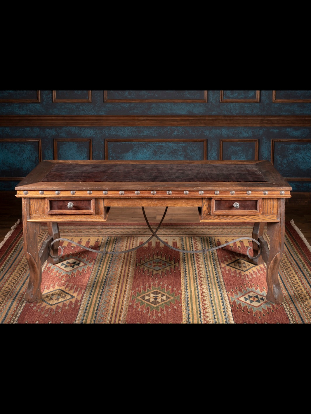 Wooden desk with drawers in a room with patterned wallpaper and rug.