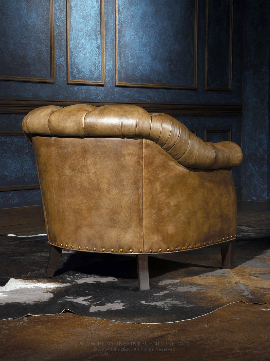 Rear view of a classic leather club chair with a softly rounded back and low-profile silhouette, finished in smooth, western-toned leather with nailhead accents along the base.