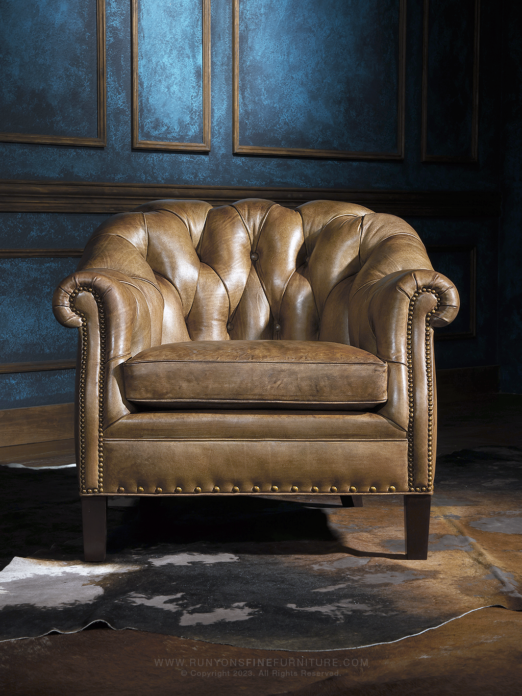 Front-facing western Chesterfield chair with deep channel tufting, plush seat cushion, and bold rolled arms. The aged saddle leather finish and brass nailheads deliver timeless rustic elegance.