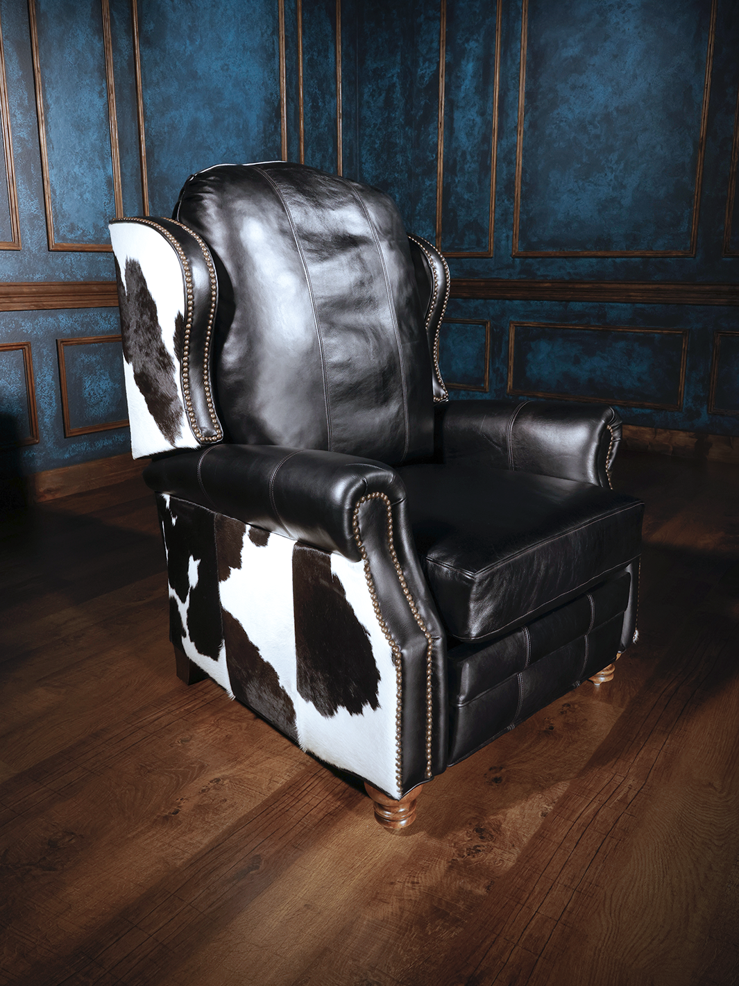 A black leather recliner with cowhide detailing on the arms and backrest, set against a room with blue walls.