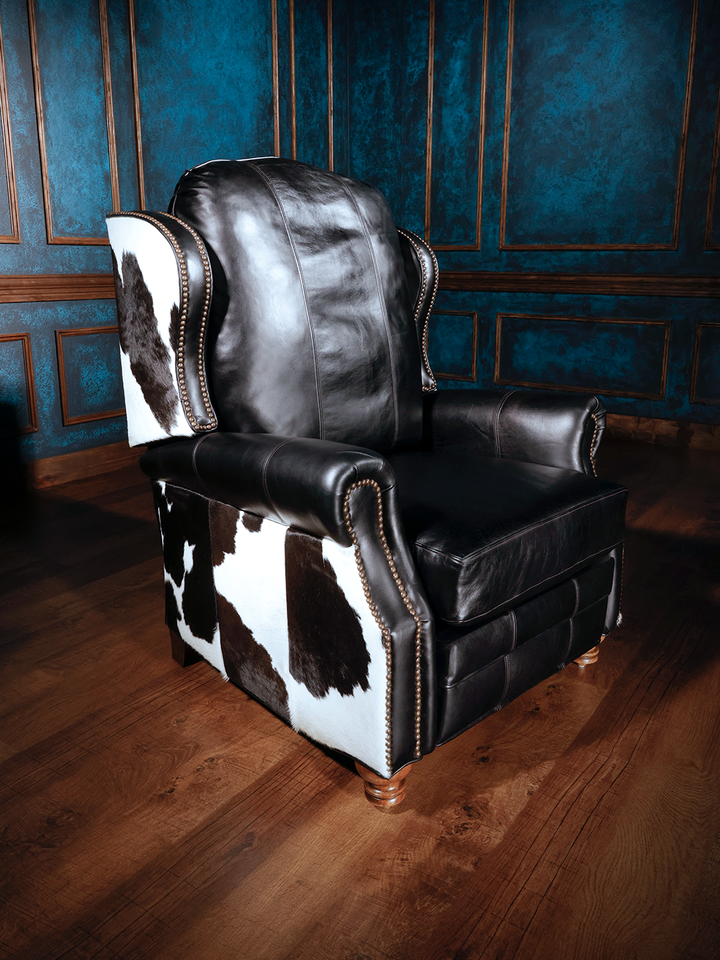 A black leather recliner with cowhide detailing on the arms and backrest, set against a room with blue walls.