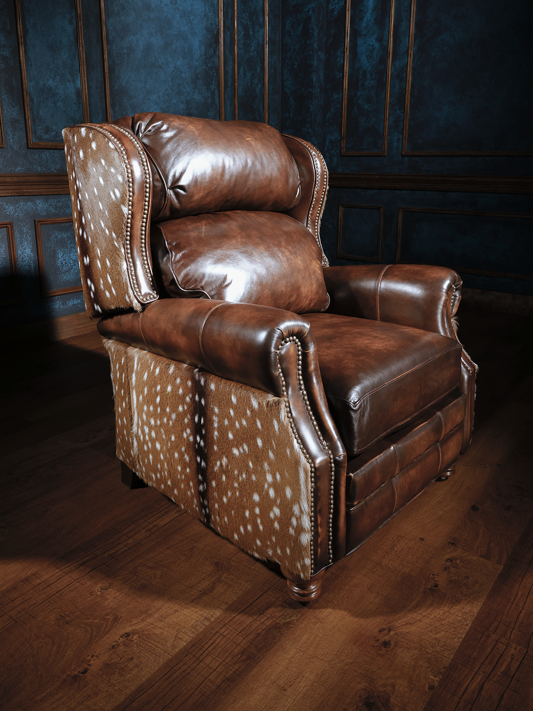 A brown leather recliner chair with patterned details on the backrest, situated in a room with wooden flooring and blue walls.