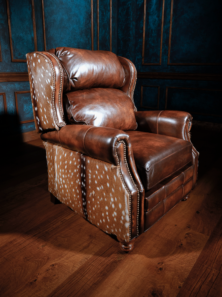 A brown leather recliner chair with patterned details on the backrest, situated in a room with wooden flooring and blue walls.
