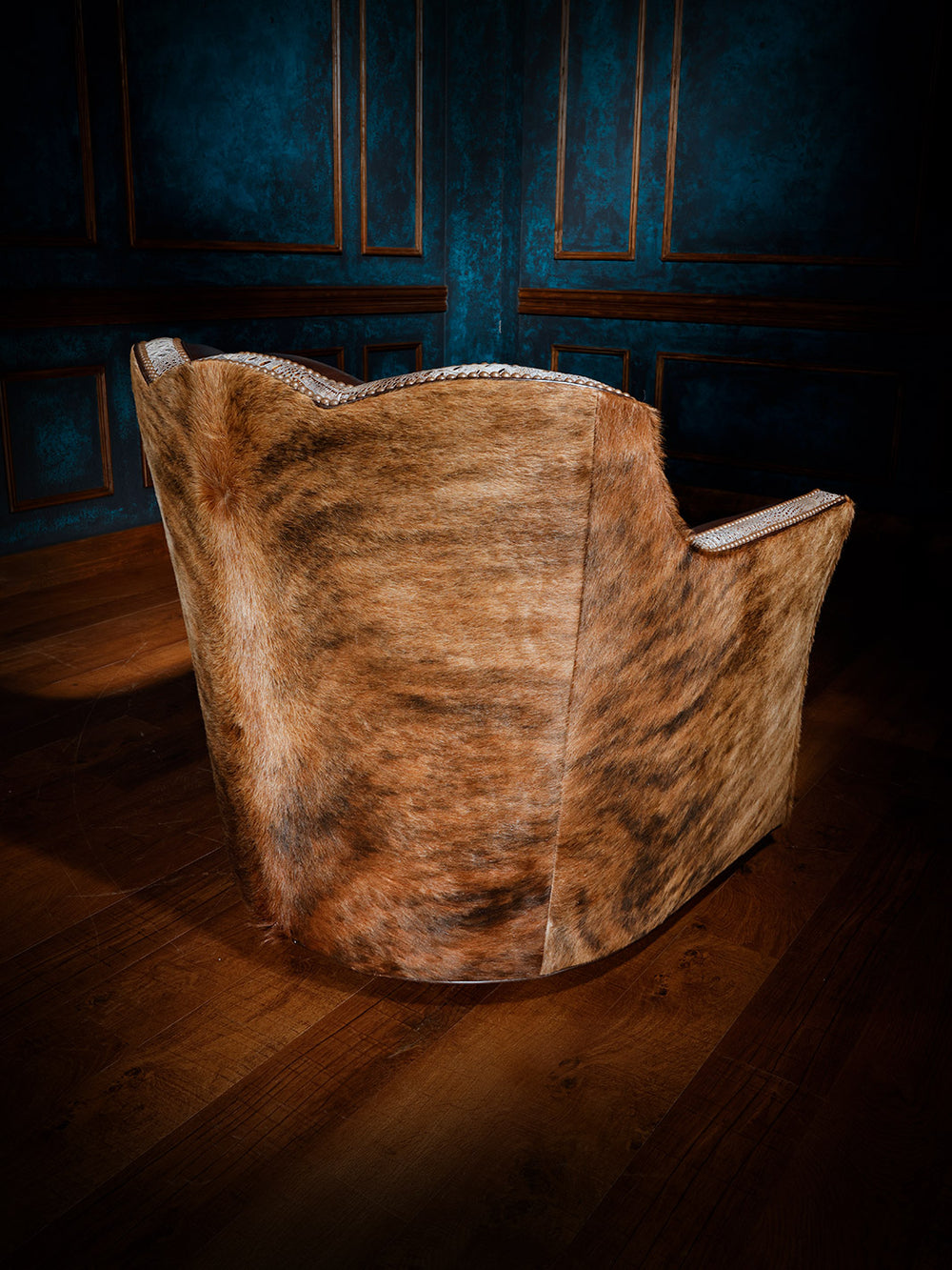 Back view of a western-style swivel chair fully upholstered in hair-on-hide with detailed nailhead trim along the edges.
