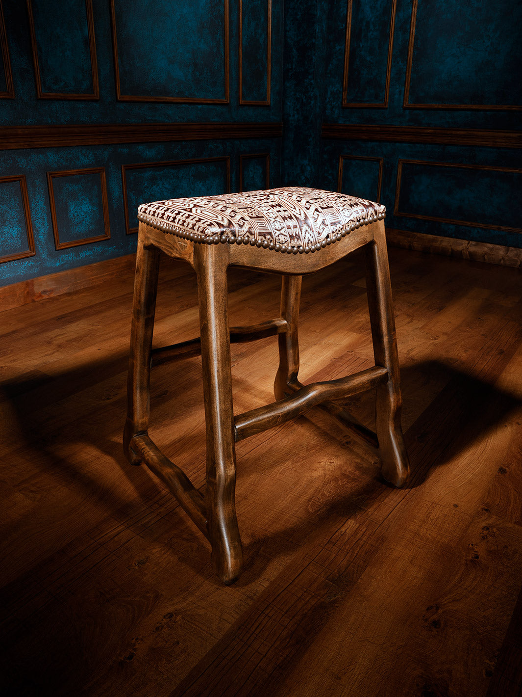 a western saddle stool featuring a tooled leather seat with intricate western patterns, accented with nailhead trim and sturdy wooden legs, no back