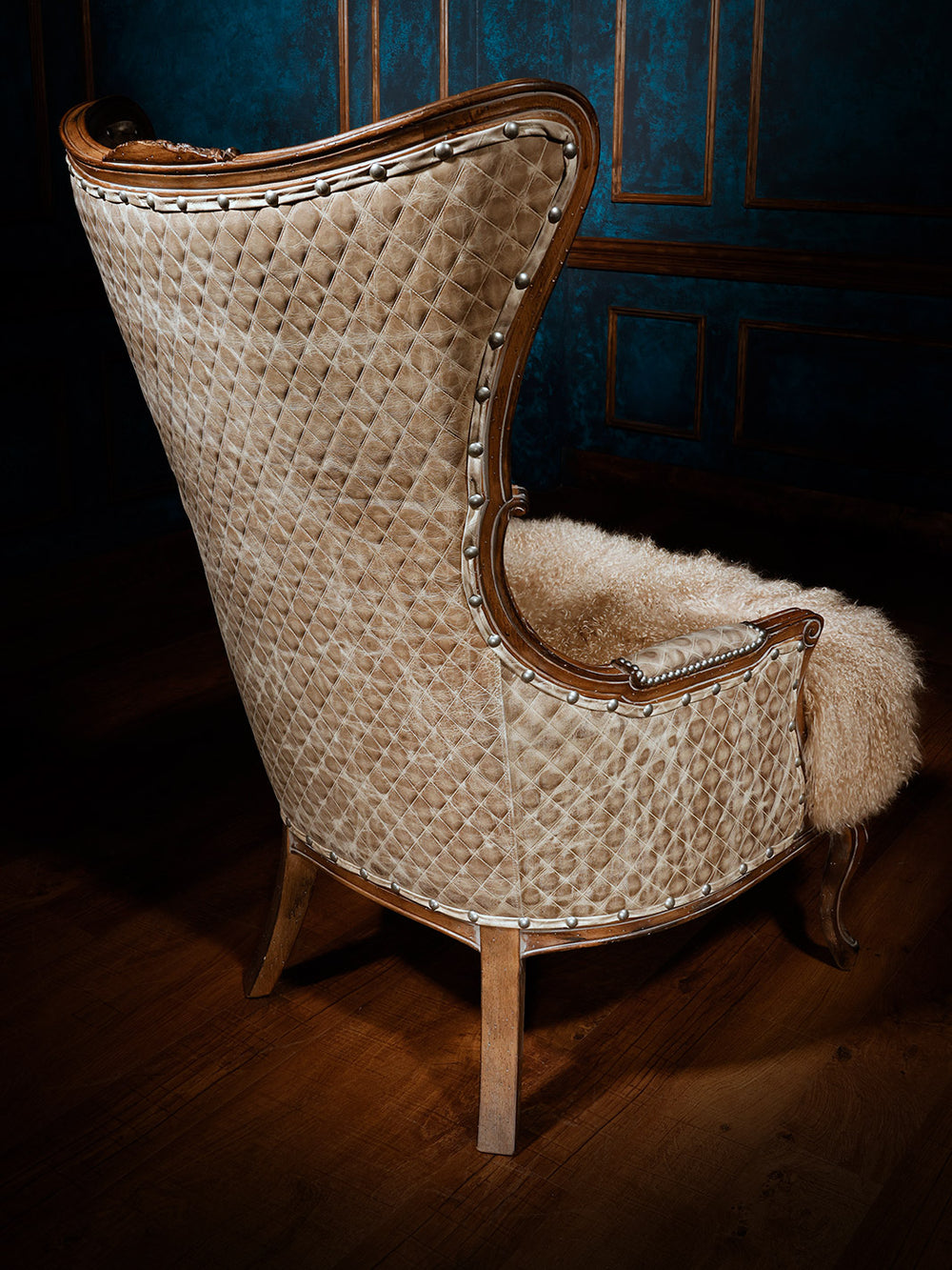 The back of the chair showcases the same diamond-quilted cream hide upholstery with decorative silver nailhead trim and curved wooden legs.