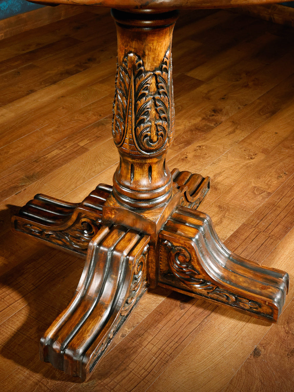Close-up of the carved wooden pedestal base of the pub table, highlighting intricate leaf and scroll motifs with a warm antique finish.