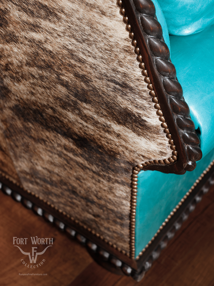 Close-up of a turquoise leather western sofa with cowhide panel and twisted carved wood detailing, highlighting the fine upholstery and nailhead trim.
