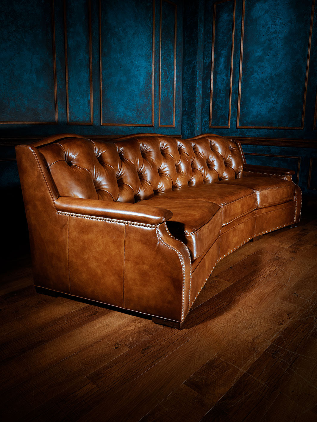 Angled view of a Western-style brown leather sofa featuring elegant curves, button-tufted back, and nailhead trim, highlighting the smooth leather finish and structured silhouette. Perfect for rustic or upscale lodge-inspired interiors.