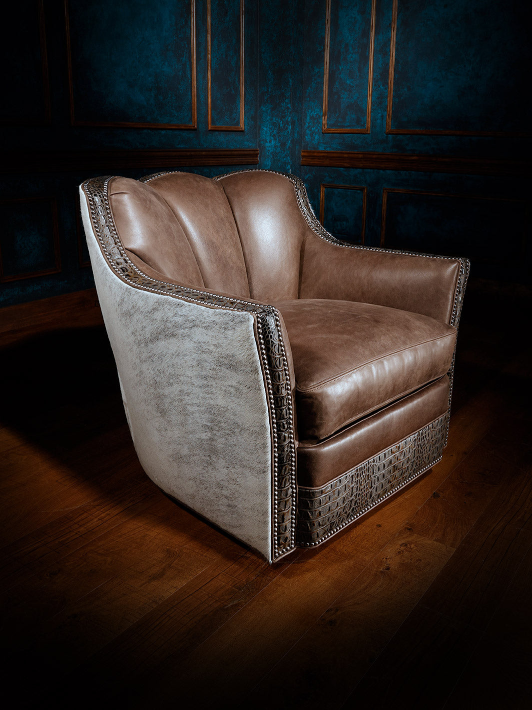 A brown and gray free range western swivel chair with cowhide leather, featuring crocodile embossed leather trim, positioned in a room with blue panel walls.