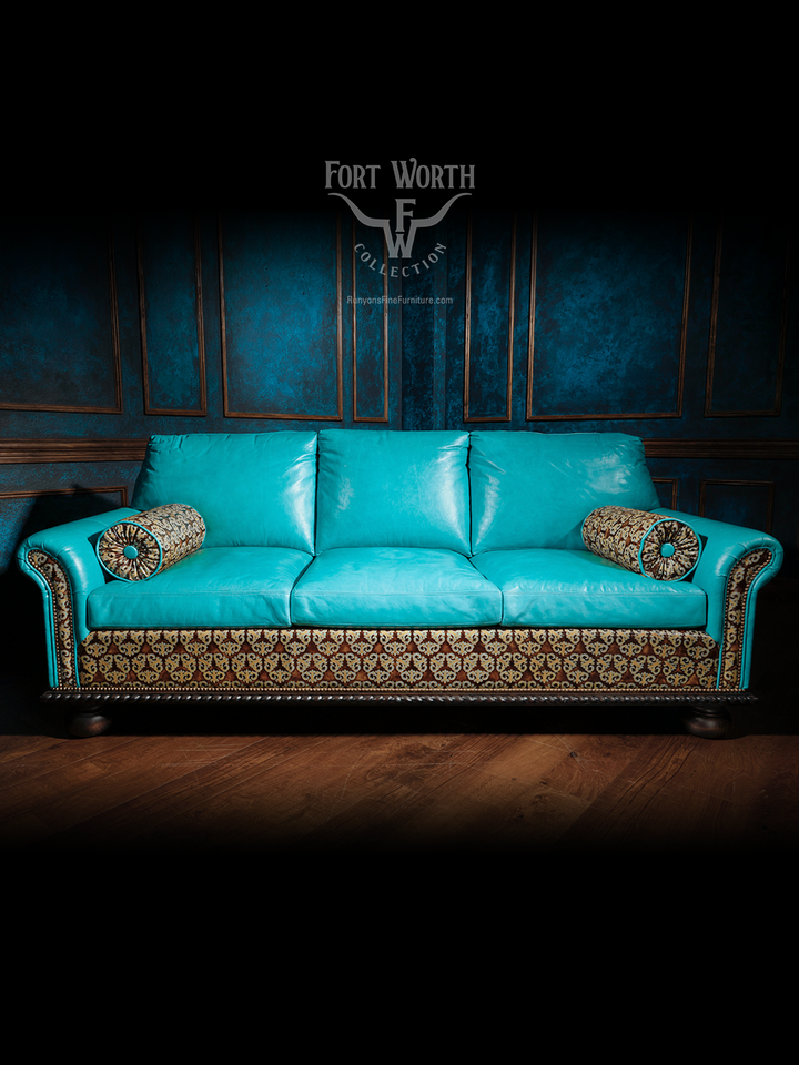 Front-facing shot of a turquoise leather western sofa with decorative bolster pillows and patterned fabric paneling, set against a blue paneled wall.