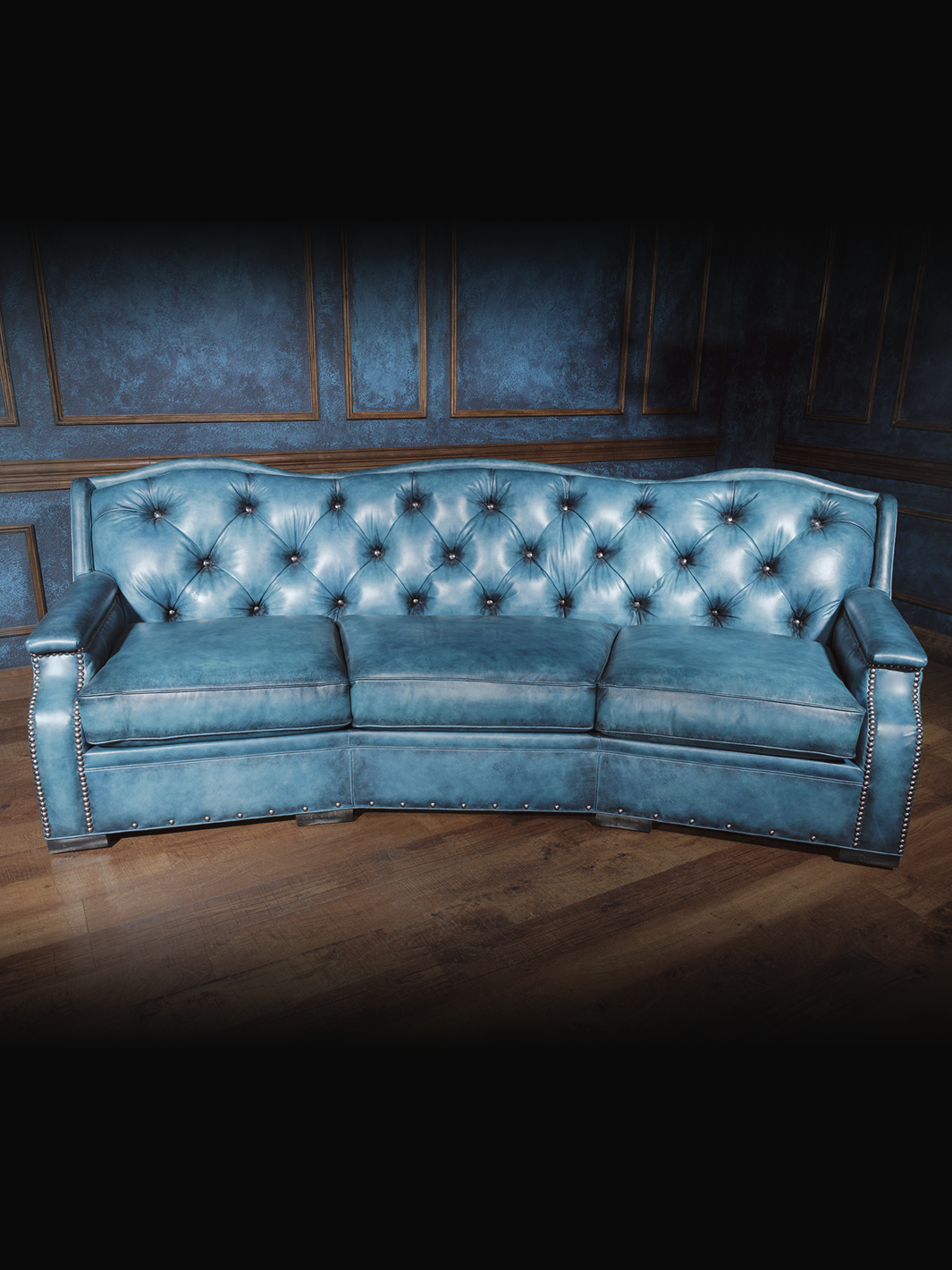 Curved turquoise blue leather sofa with button-tufted backrest and silver nailhead trim, styled in a western interior setting.