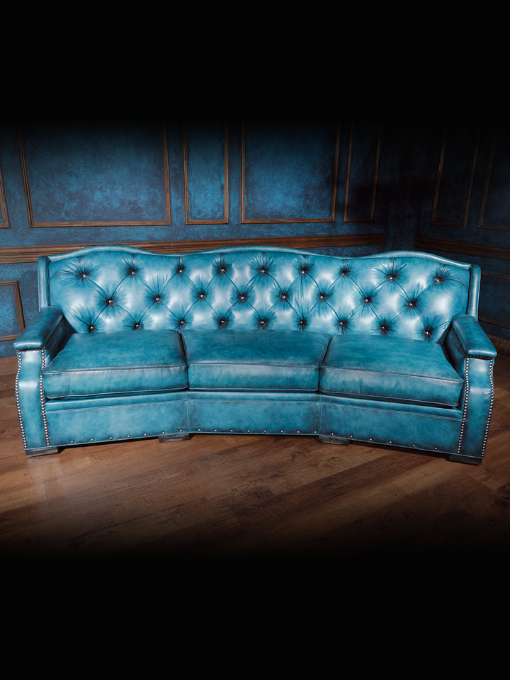 Curved turquoise blue leather sofa with button-tufted backrest and silver nailhead trim, styled in a western interior setting.
