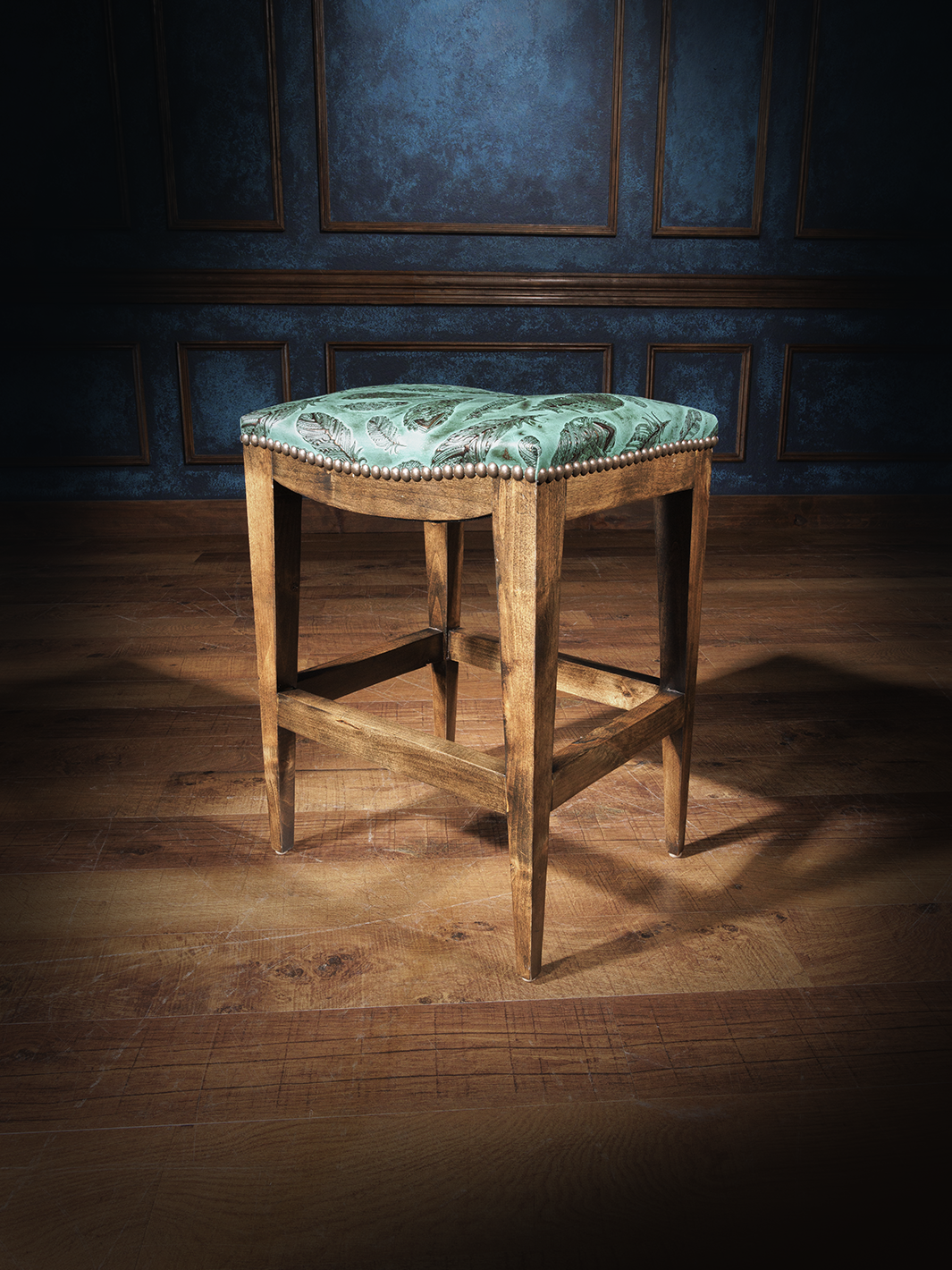 A handcrafted leather saddle stool with a green floral pattern on the seat, a brown wooden frame, and a tufted backrest.
