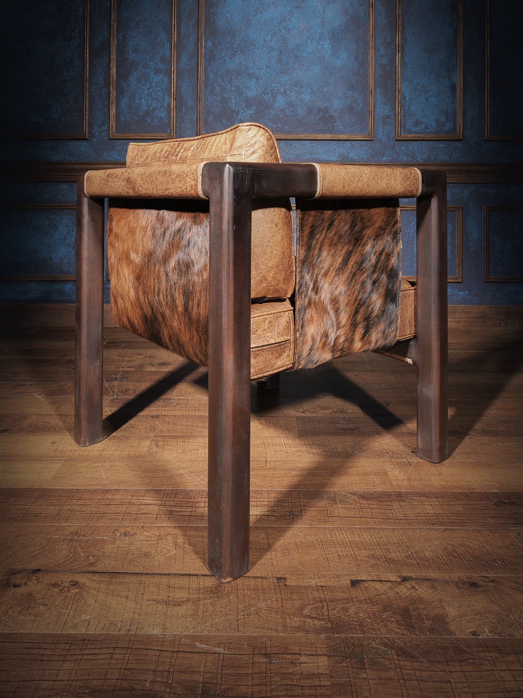 Western Santa Fe sling chair with a rich wooden frame and panels of warm distressed leather and brindle cowhide. The chair’s back and seat sling subtly into the frame, offering a blend of southwestern charm and contemporary form.