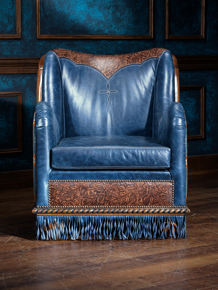 Western fringe leather accent chair in rich blue leather with tooled leather panels, contrast stitching, and decorative fringe along the base. The upper back features a carved leather insert and subtle embroidered detailing.