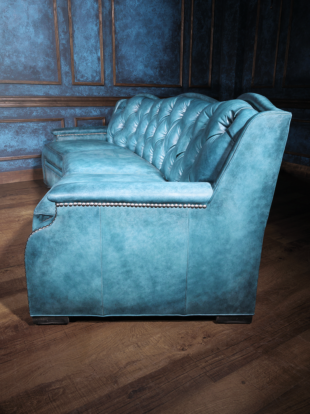 Side view of a vibrant blue leather western-style sofa showcasing curved backrest design and detailed nailhead accents.