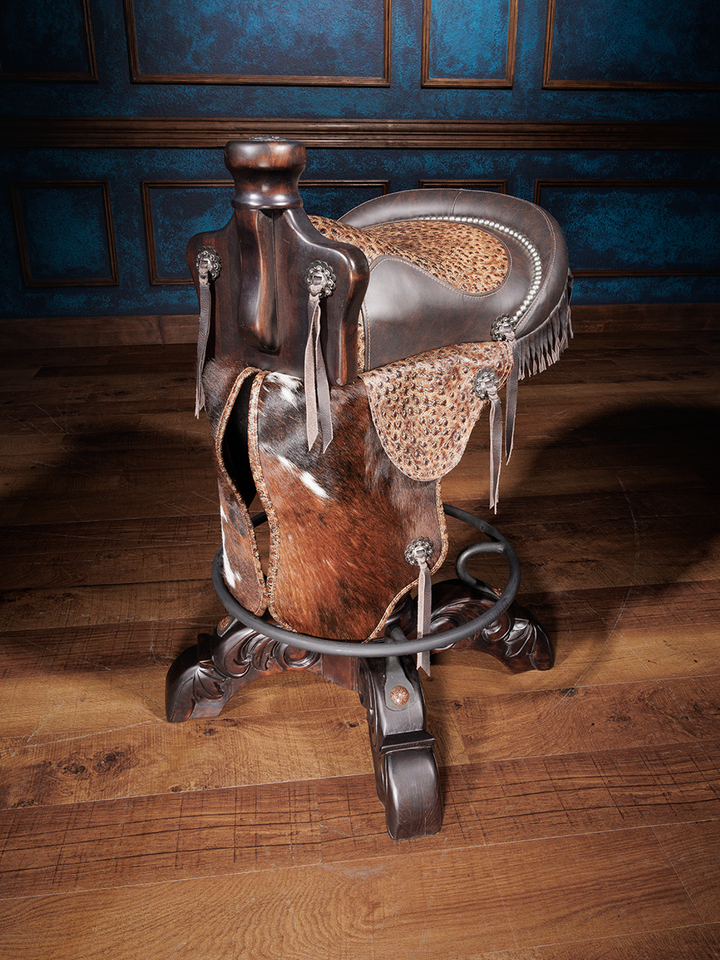 A saddle bar stool with dark brown full-grain leather and mocha-colored genuine leather with ostrich embossing. It features silver-finished conchos, hand tacks, and cowhide in the saddle's fenders, seat, and flaps.