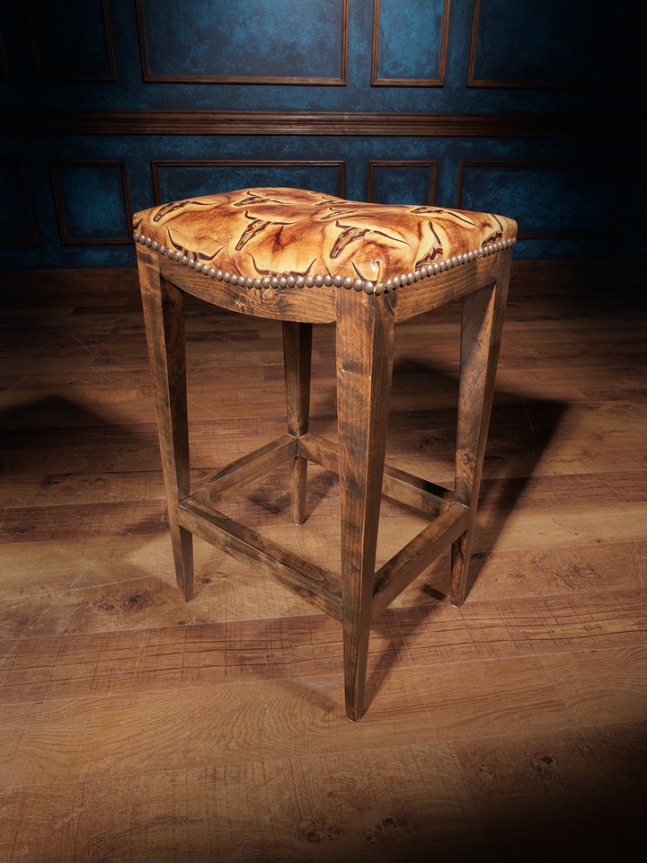 A saddle stool with a brown wooden frame and an upholstered seat featuring a geometric pattern, likely designed with themes from the Old West.