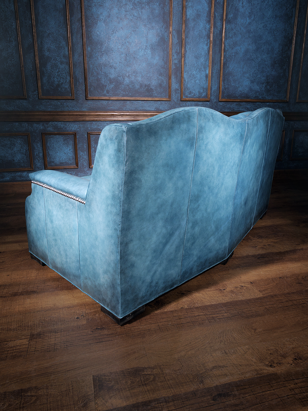 Back view of a bright blue western leather couch featuring a high, scalloped back and smooth paneling on hardwood floors.