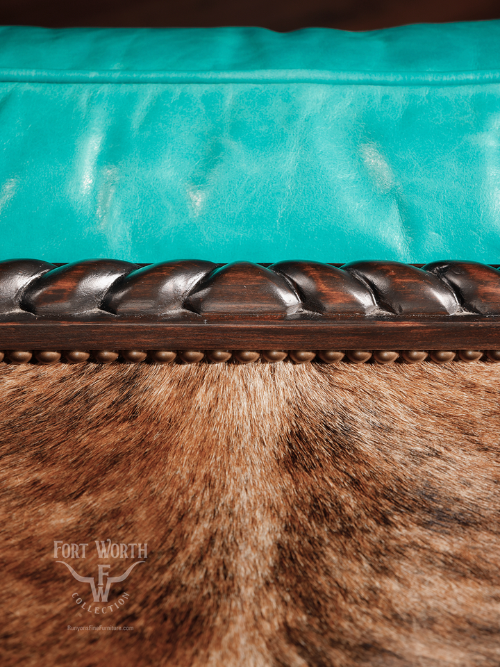 Detail shot of a turquoise leather cushion bordered by carved wood trim and brown cowhide, showcasing luxurious textures in a western-inspired design.