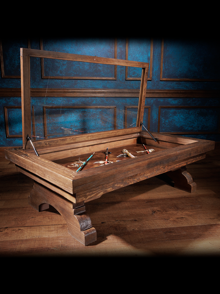 An exquisite hand-tooled leather coffee table with a glass top and wooden frame, displayed against a blue panelled wall.