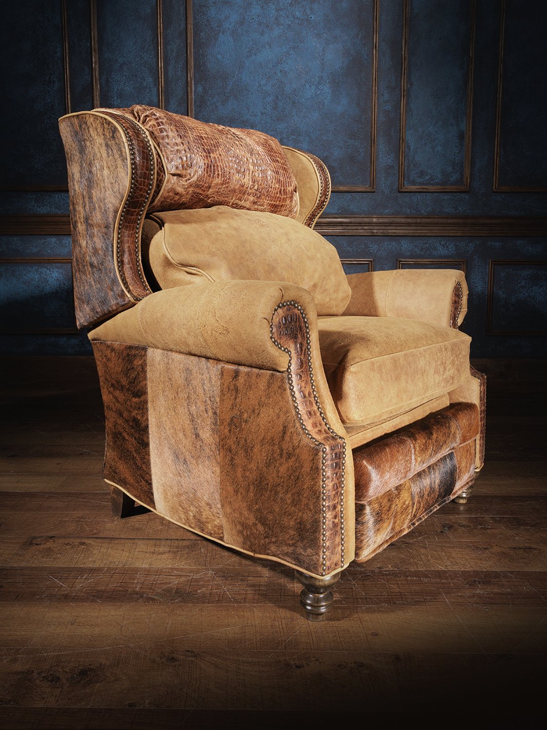A leather recliner with a crocodile pattern on the top cushion and cowhide on the outside back, set against a dark blue textured wall.