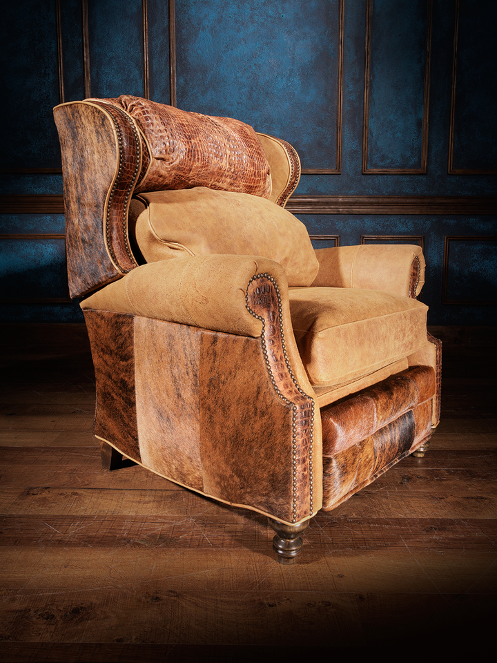 A leather recliner with a crocodile pattern on the top cushion and cowhide on the outside back, set against a dark blue textured wall.
