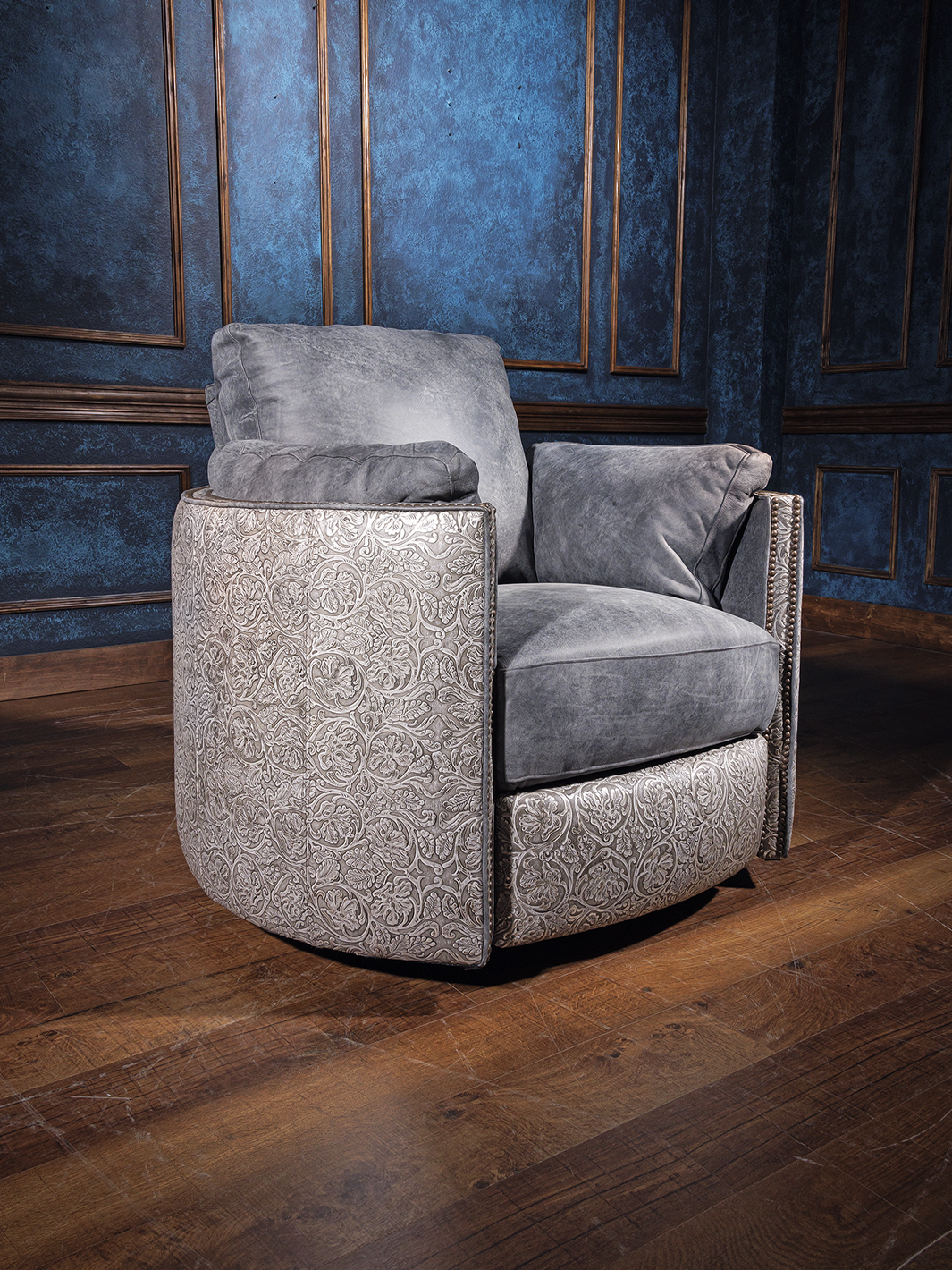 A gray leather snug swivel recliner chair placed on a wooden floor with a blue textured wall in the background.